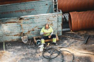 Ouvrier en uniforme de sécurité assis sur un banc, entouré d'équipements de construction.