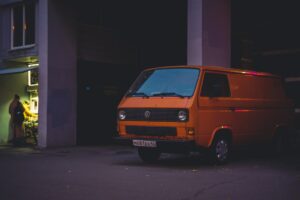 Fourgonnette Volkswagen orange garée dans une rue sombre.