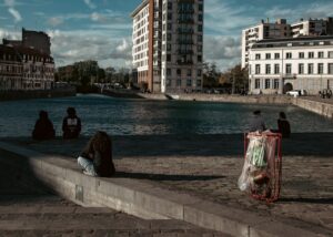 Vue de personnes assises sur un ponton au bord de l'eau avec bâtiments en arrière-plan à Lille, près d'un volet roulant exist