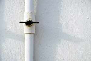 Tuyau blanc avec valve noire sur mur blanc texturé.