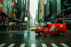 Scène animée de Times Square à New York, avec des panneaux publicitaires, des taxis et un camion Coca-Cola.