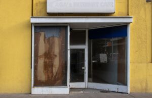 Façade jaune délabrée avec porte et fenêtre endommagées.
