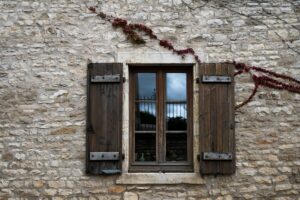 Fenêtre en bois rustique avec volets et plantes grimpantes.