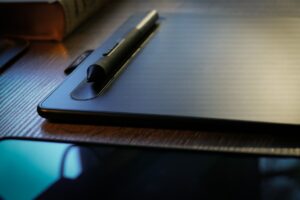 Tablette graphique noire avec stylet sur bureau en bois.